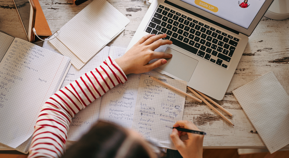 student exercise books over the table , pencils , laptop , left index finger over the laptop, touch pad