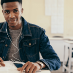 african student , wearing a blue jean jacket, mobile device , headphones , exercise book , pen