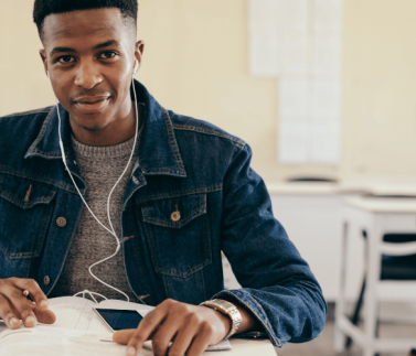 african student , wearing a blue jean jacket, mobile device , headphones , exercise book , pen