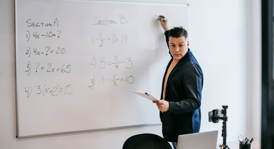 teacher writing on the white board , using a black marker , mobile device , laptop