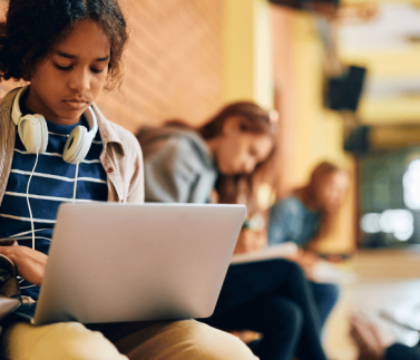 black girl leaning next to the red face brick building , laptop , white headphones