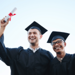 2 male graduate , black and white, holding white papers tied with red ribbon,